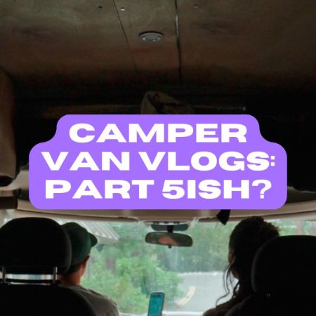 Two people sitting in the front seat of a van, shown from behind, looking out the front windshield.