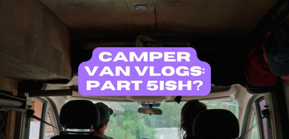 Two people sitting in the front seat of a van, shown from behind, looking out the front windshield.